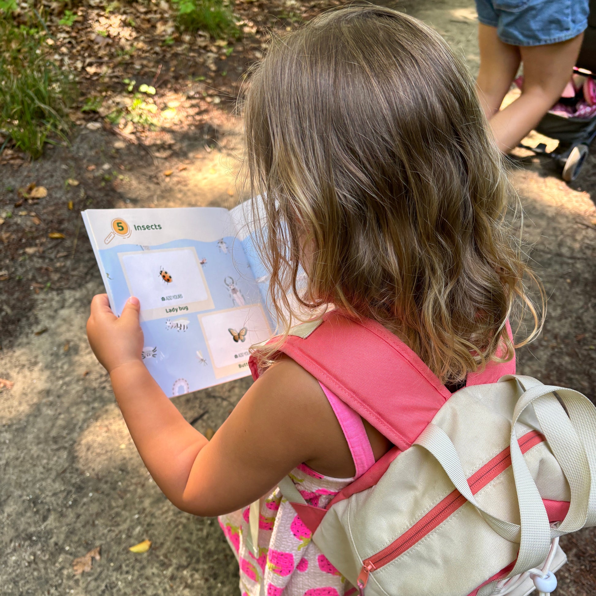 Child with a backpack reading a book outdoors