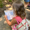 Child with a backpack reading a book outdoors