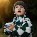 Child wearing a checkered coat and knit hat, holding a toy camera outdoors.
