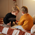 Two children sitting on a bed in a bedroom setting.